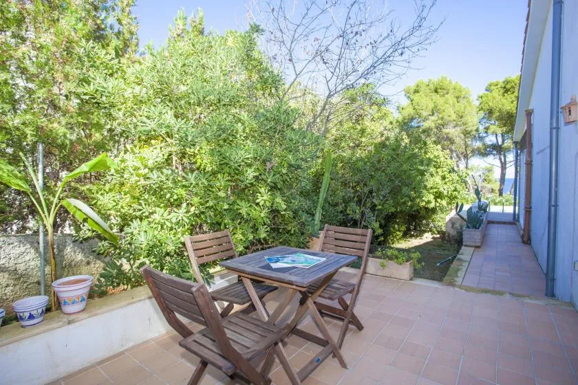 A tiled patio with a wooden dining set beside leafy garden plants.