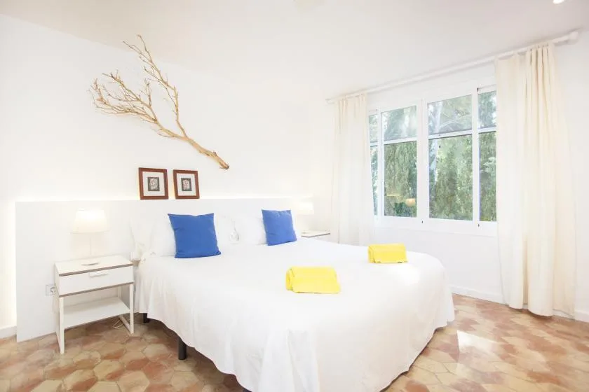 A bright bedroom with a white bed and large windows.