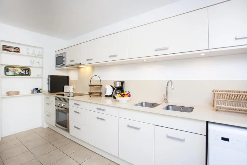 A bright white kitchen with long countertops, cabinets, and a sink.