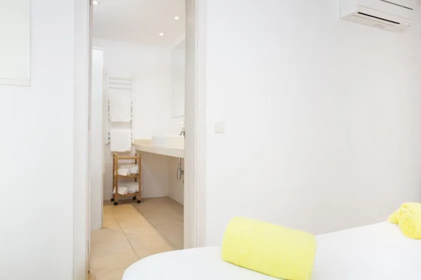 A bright bedroom with a bed and an adjoining bathroom visible through the doorway.
