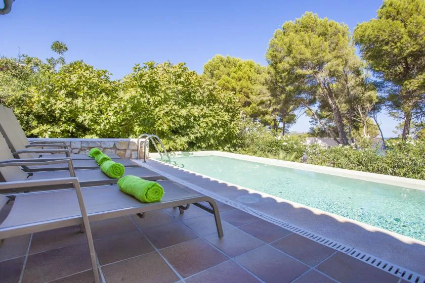 A swimming pool beside a tiled patio with lounge chairs and green towels.