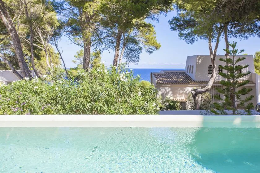 A swimming pool sits among trees, with the sea visible beyond.