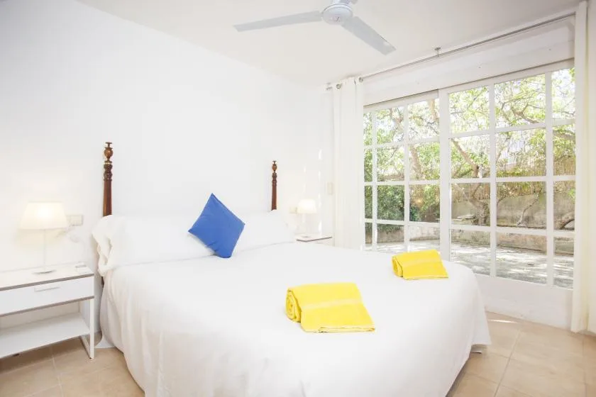 A bright bedroom with a white bed and large windows overlooking greenery.