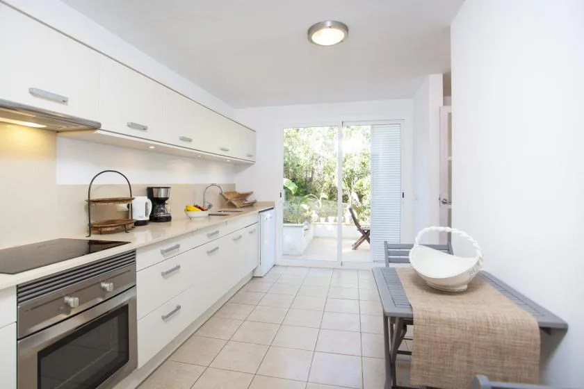 A bright kitchen with white cabinets and a glass door opening onto greenery.