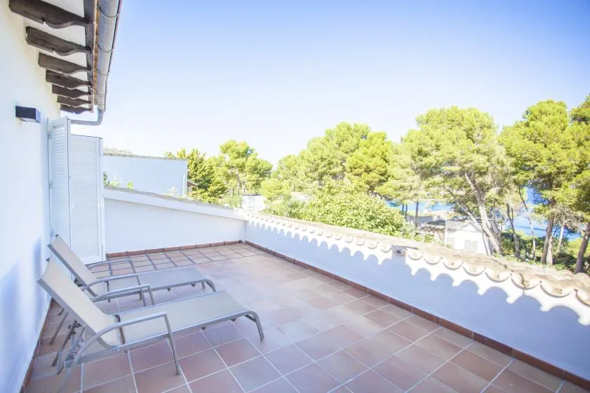A tiled outdoor terrace with reclining seating overlooks trees.