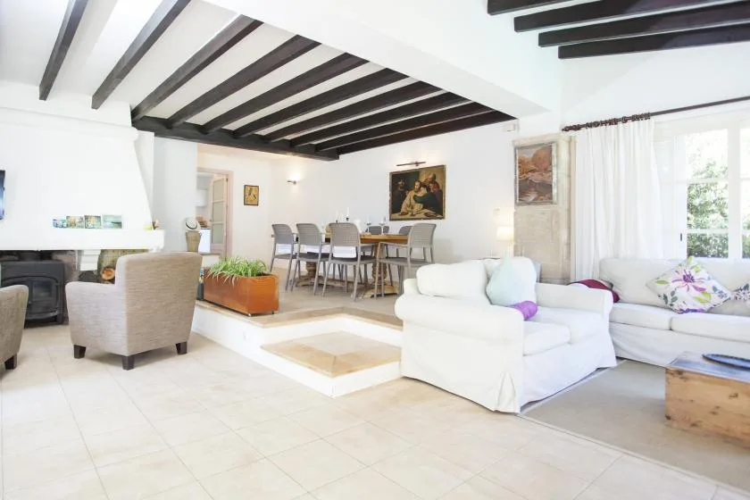 A bright living and dining area with seating, a dining table, and dark ceiling beams.