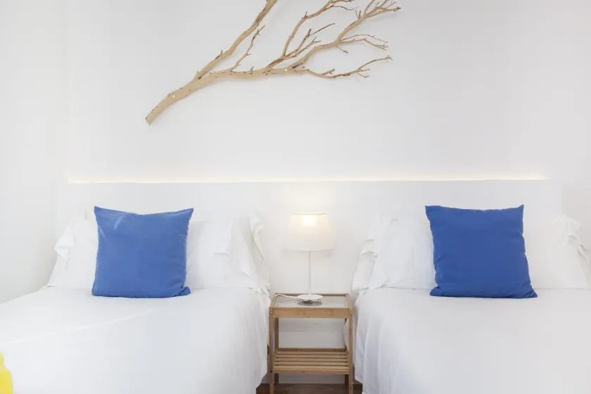 A bright bedroom with two beds and a small table between them.