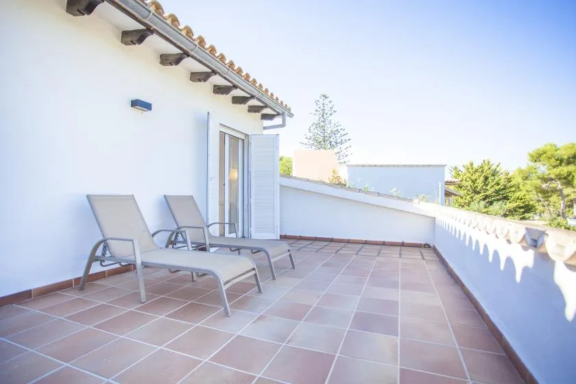 A tiled outdoor terrace with two reclining seats beside an open doorway.