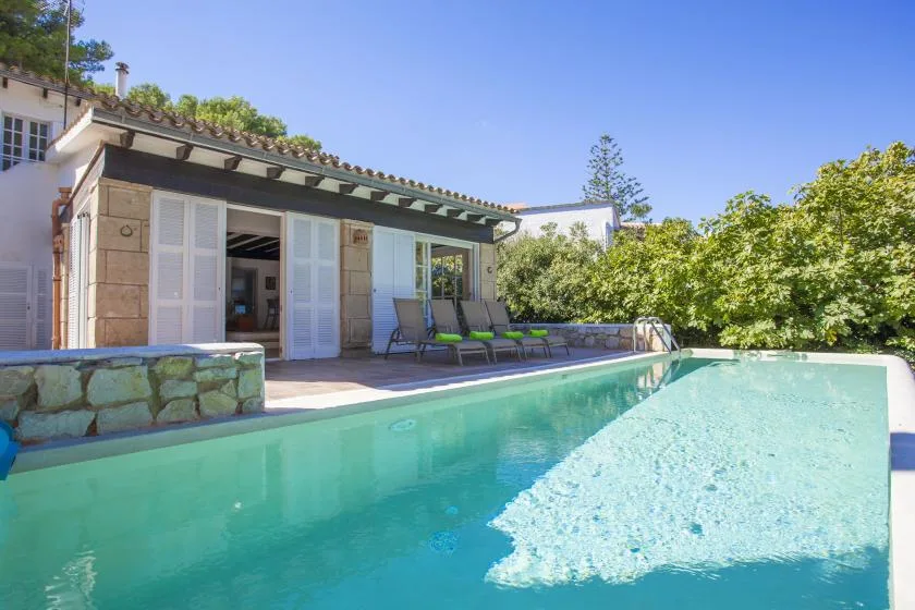 A swimming pool beside a house, with lounge seating on the patio.