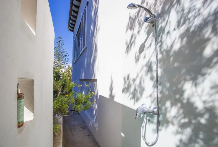 An outdoor shower stands beside a narrow passage between white and blue walls.