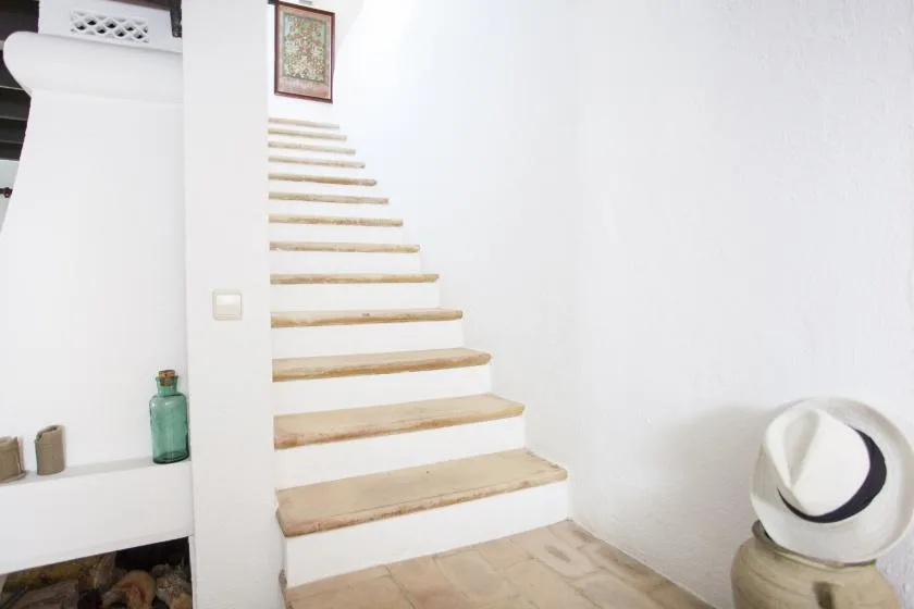 A white interior staircase with light-colored steps rises beside a plain wall.