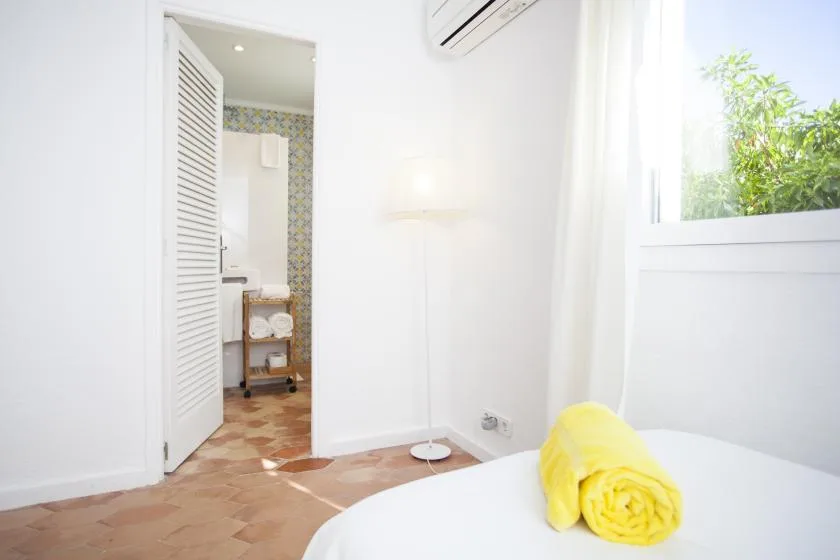 A bright bedroom with a yellow towel on the bed and an open bathroom doorway.