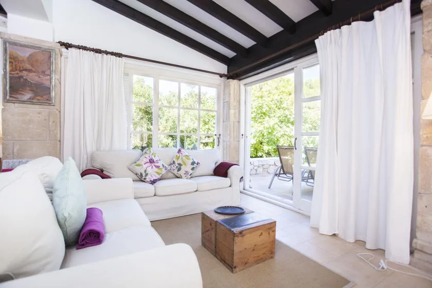 A bright living room with white seating beside large windows and an open patio door.