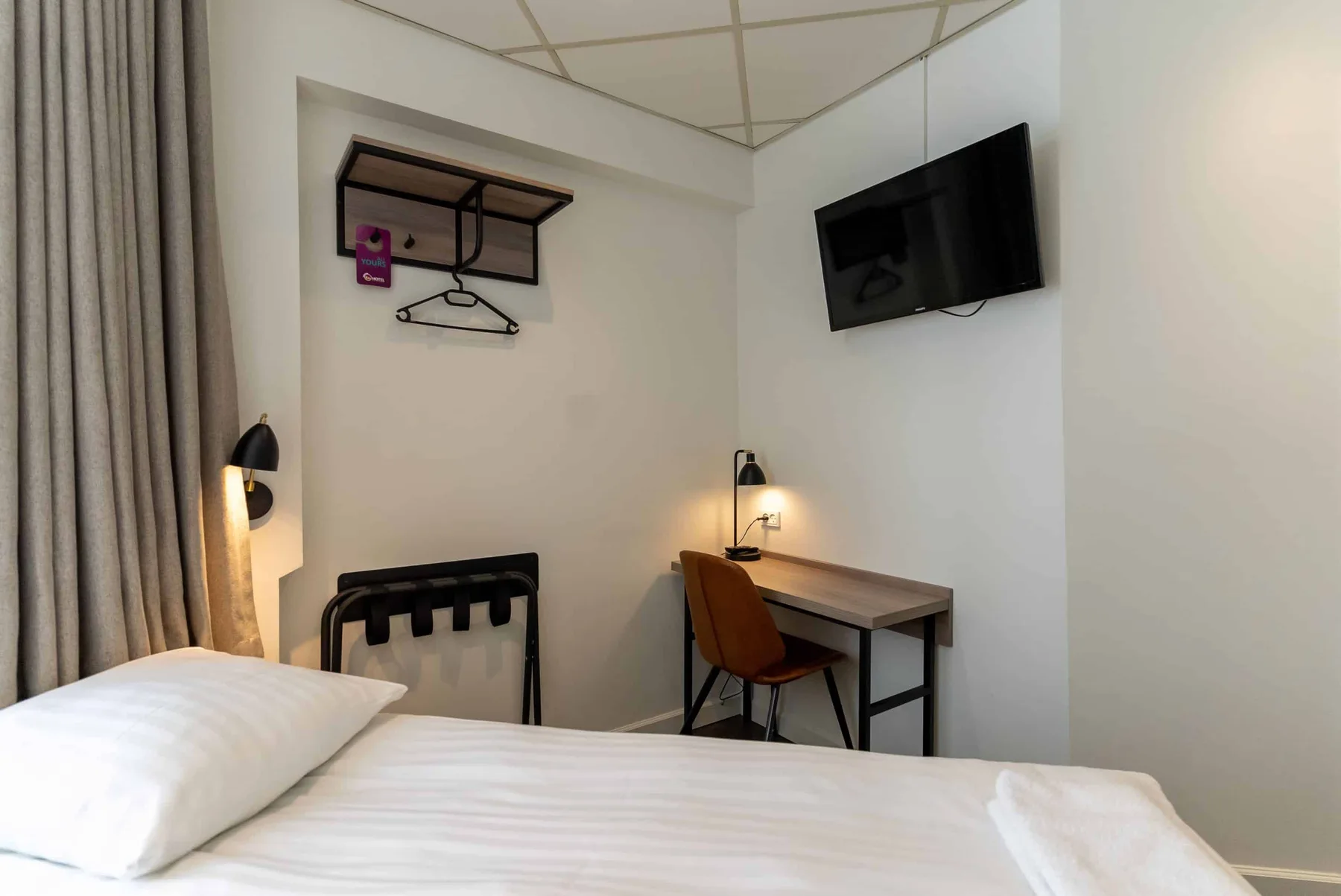 Hotel room showing a bed, TV, desk, chair, reading lamp and luggage bench.