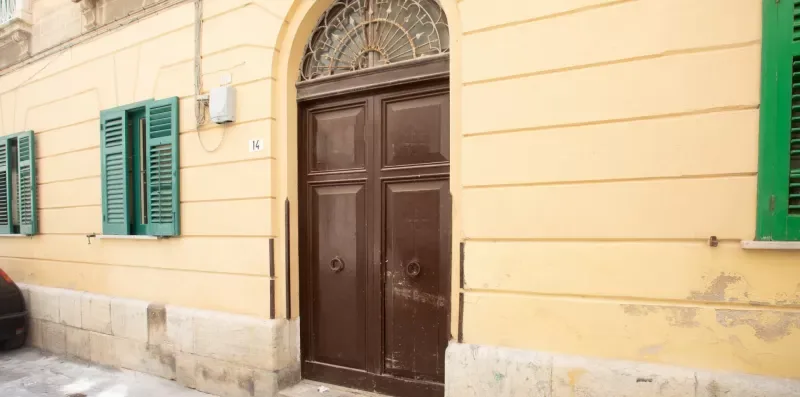 A yellow building facade with a dark wooden entrance and green shutters.