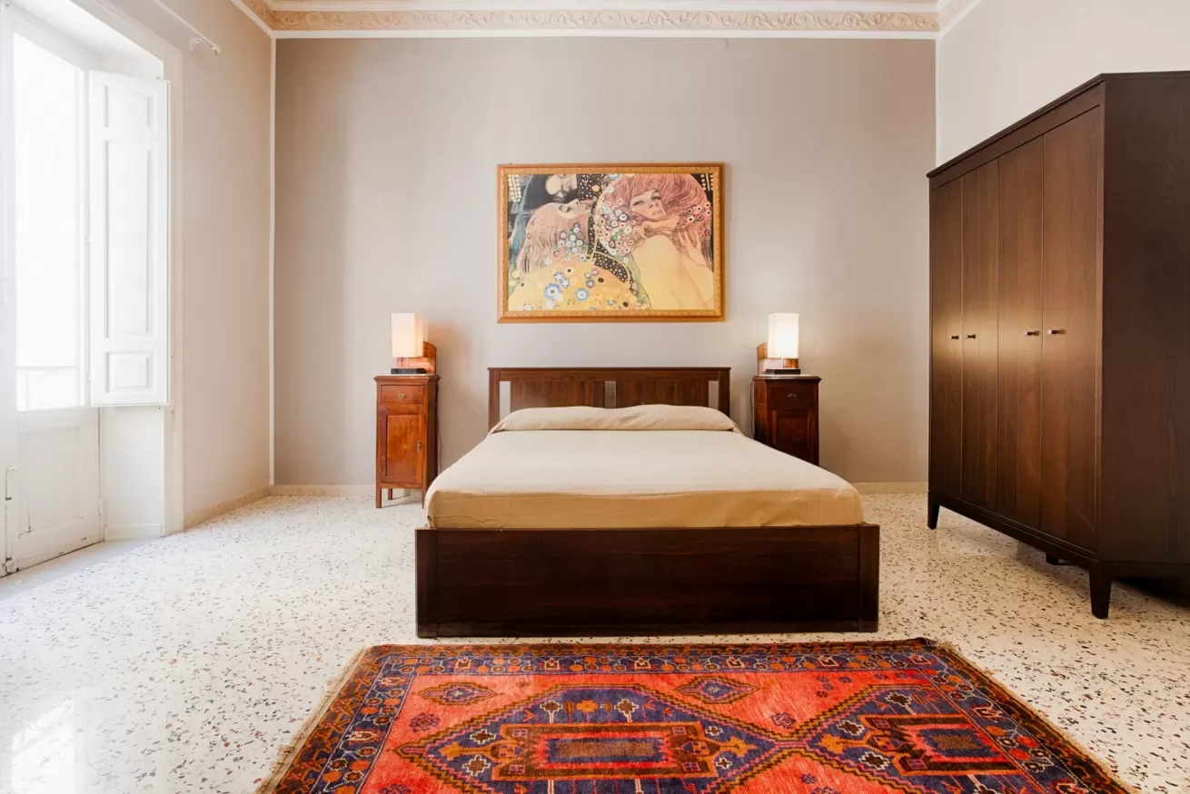 A bedroom with a dark wooden bed, matching bedside tables, and a colorful rug.