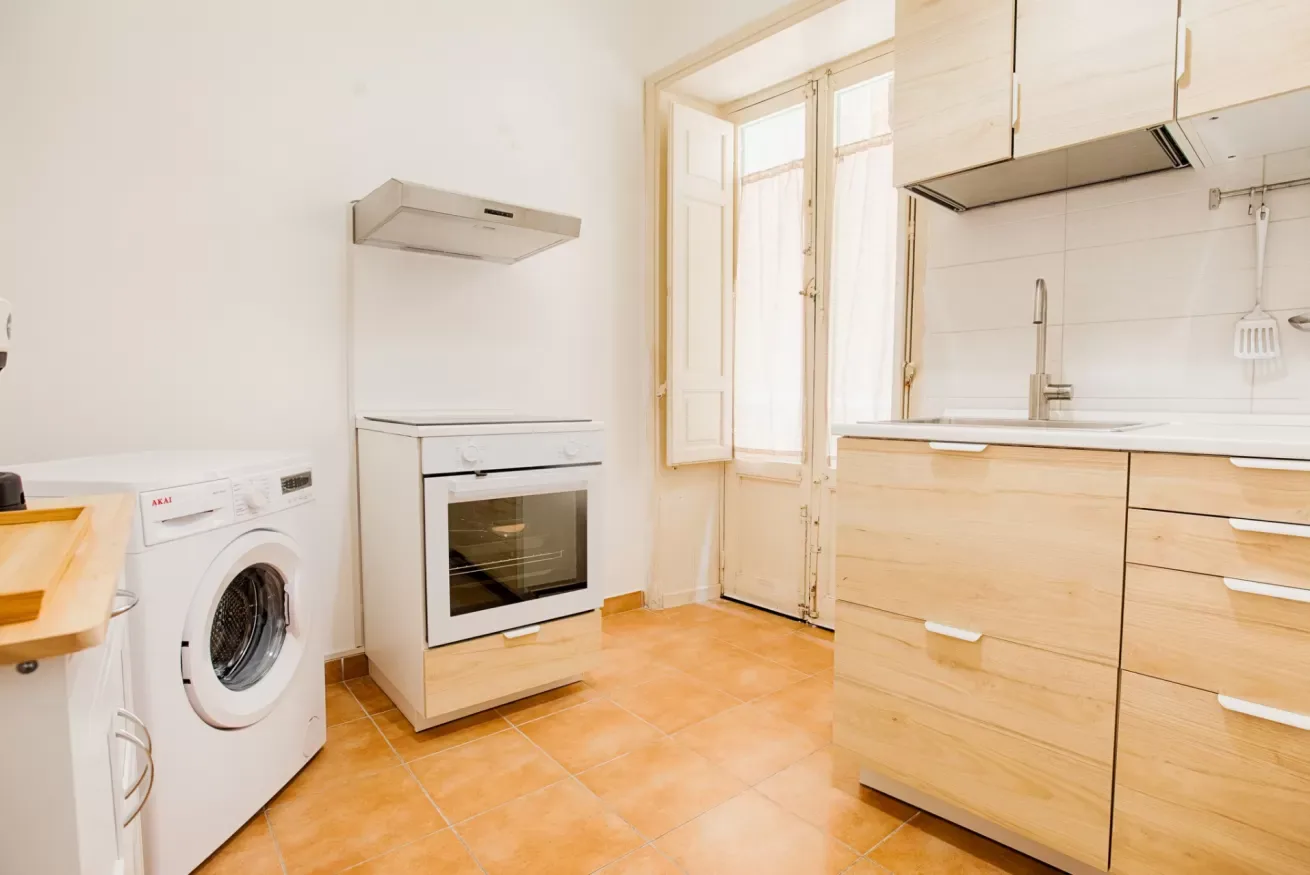 A bright kitchen with light wood cabinets, a stove, and a washing machine.