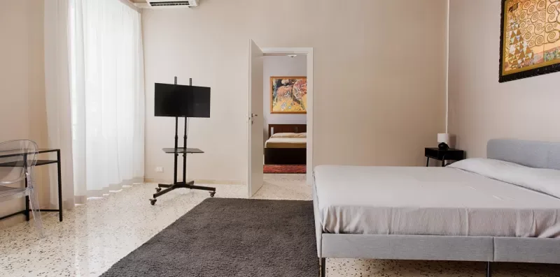 A bedroom with a low bed, television stand, and doorway to another room.