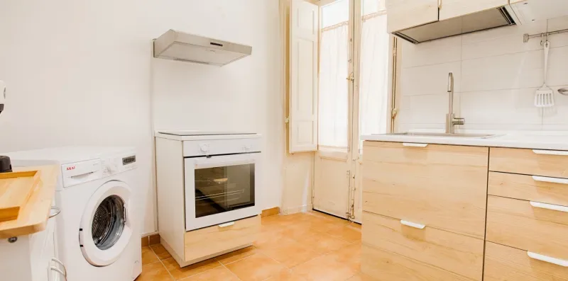 A bright kitchen with an oven, washing machine, and light wood cabinets.