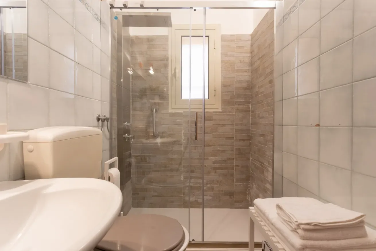 A tiled bathroom with a glass shower and a window.