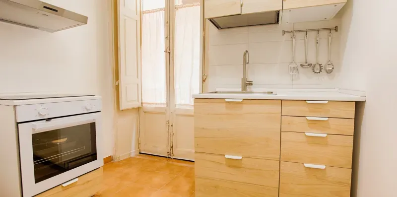A bright kitchen with pale wood cabinets, a countertop, and a built-in oven.