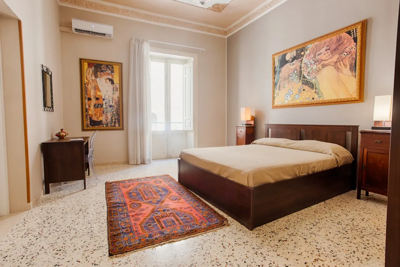 A bedroom with a large bed, colorful rug, and framed artwork.