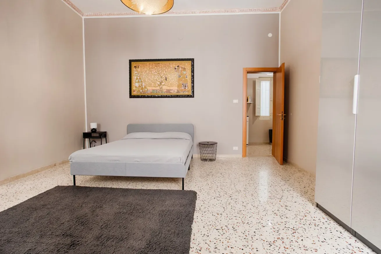 A bedroom with a bed, a framed picture, and a dark rug.