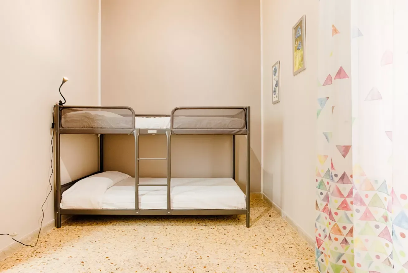 A bunk bed stands against a light wall beside a colorful patterned curtain.