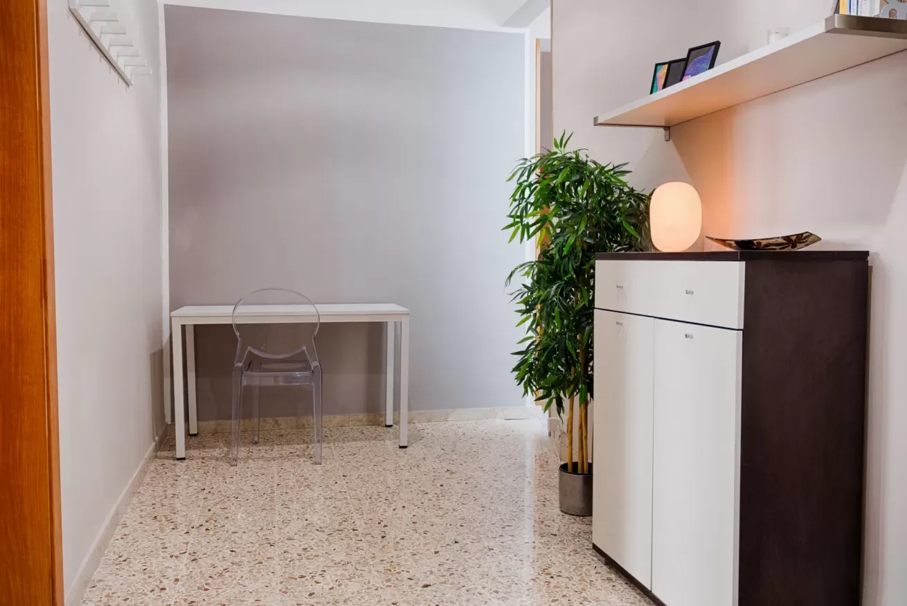 A small interior area with a desk, clear chair, potted plant, and cabinet.