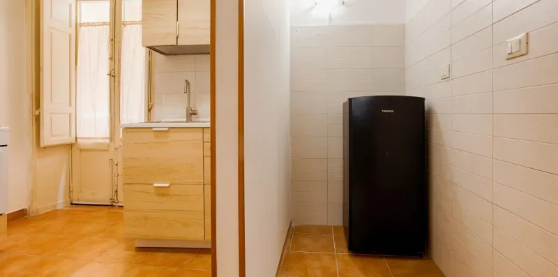 A tiled room with a black refrigerator beside a wooden kitchen counter.