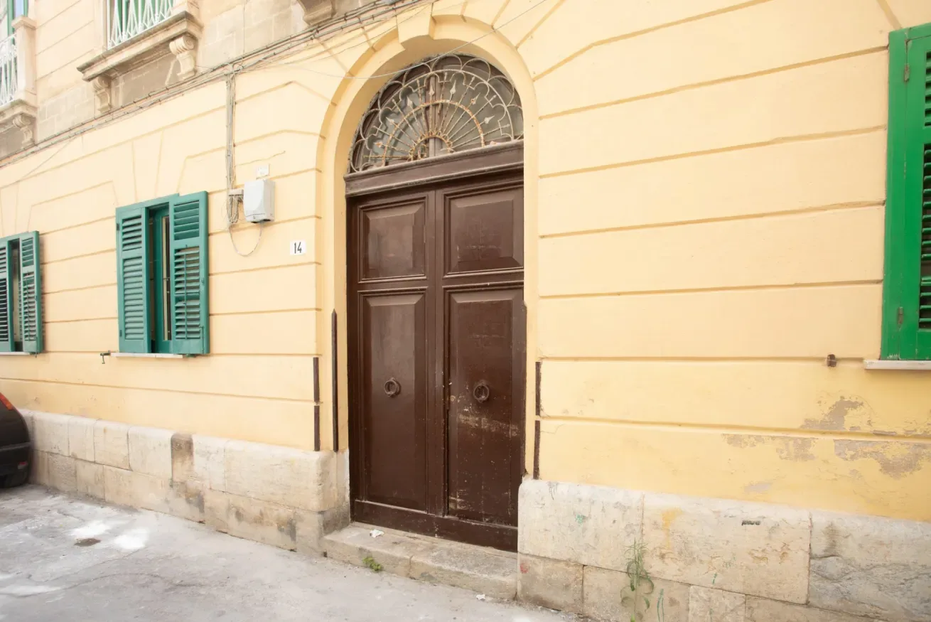 A yellow building facade with a dark wooden entrance and green shutters.