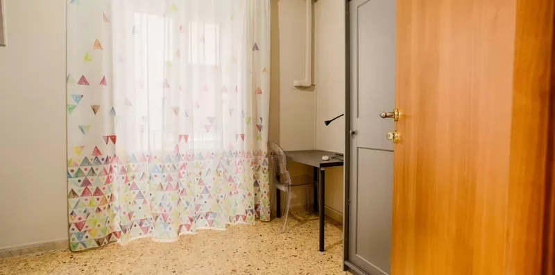 A small room with patterned curtains, a desk, and an open wooden door.