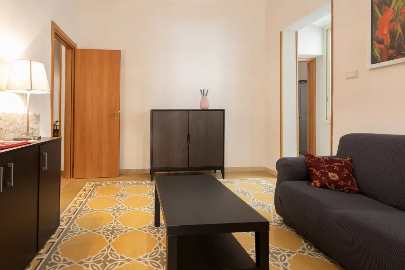 A living room with dark seating, a coffee table, and patterned floor tiles.
