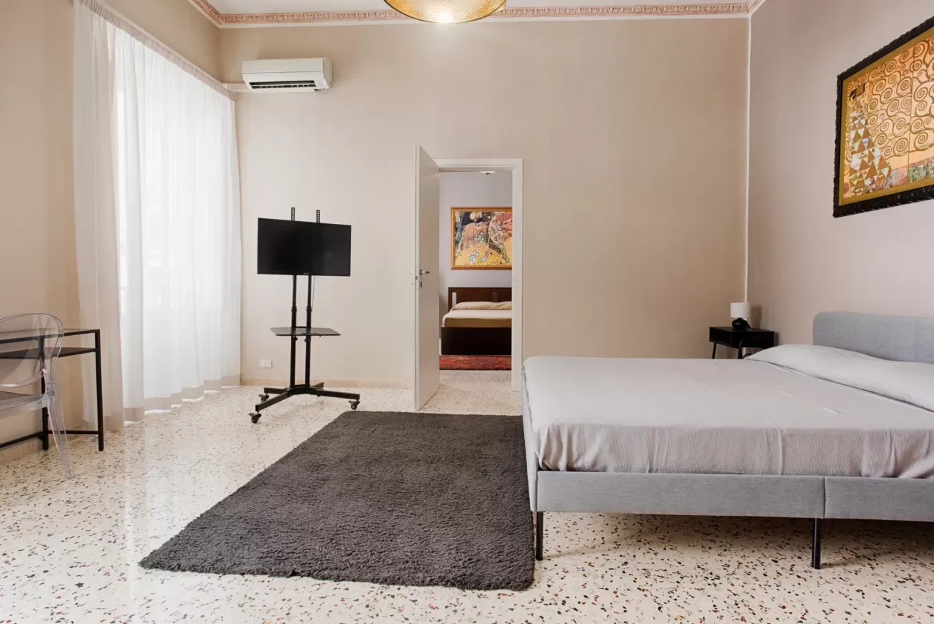 A bedroom with a bed, a dark rug, and a television near the window.