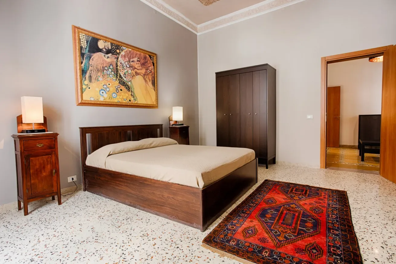 A bedroom with a wooden bed, a dark wardrobe, and a patterned rug.