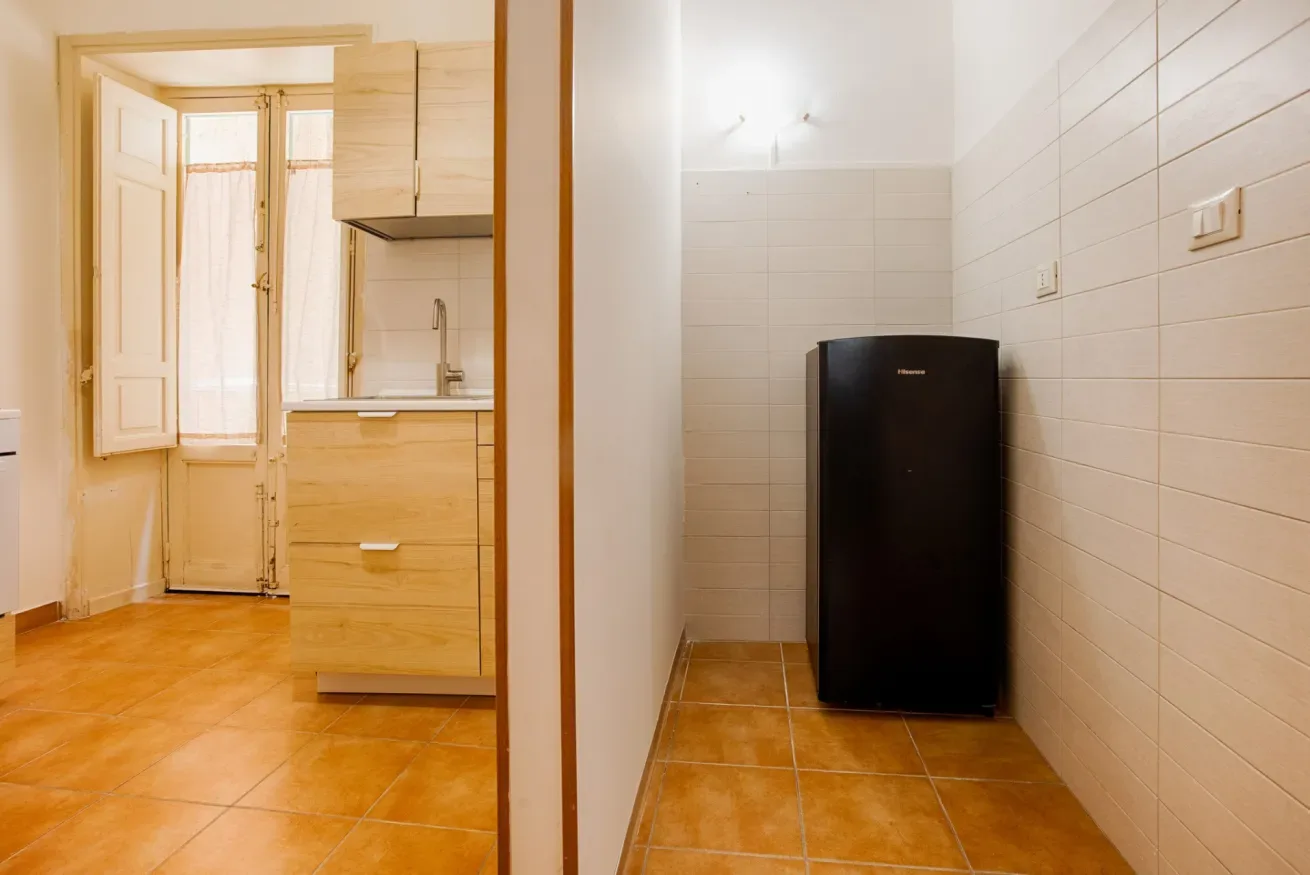 A tiled kitchenette with a black refrigerator and wooden cabinets.