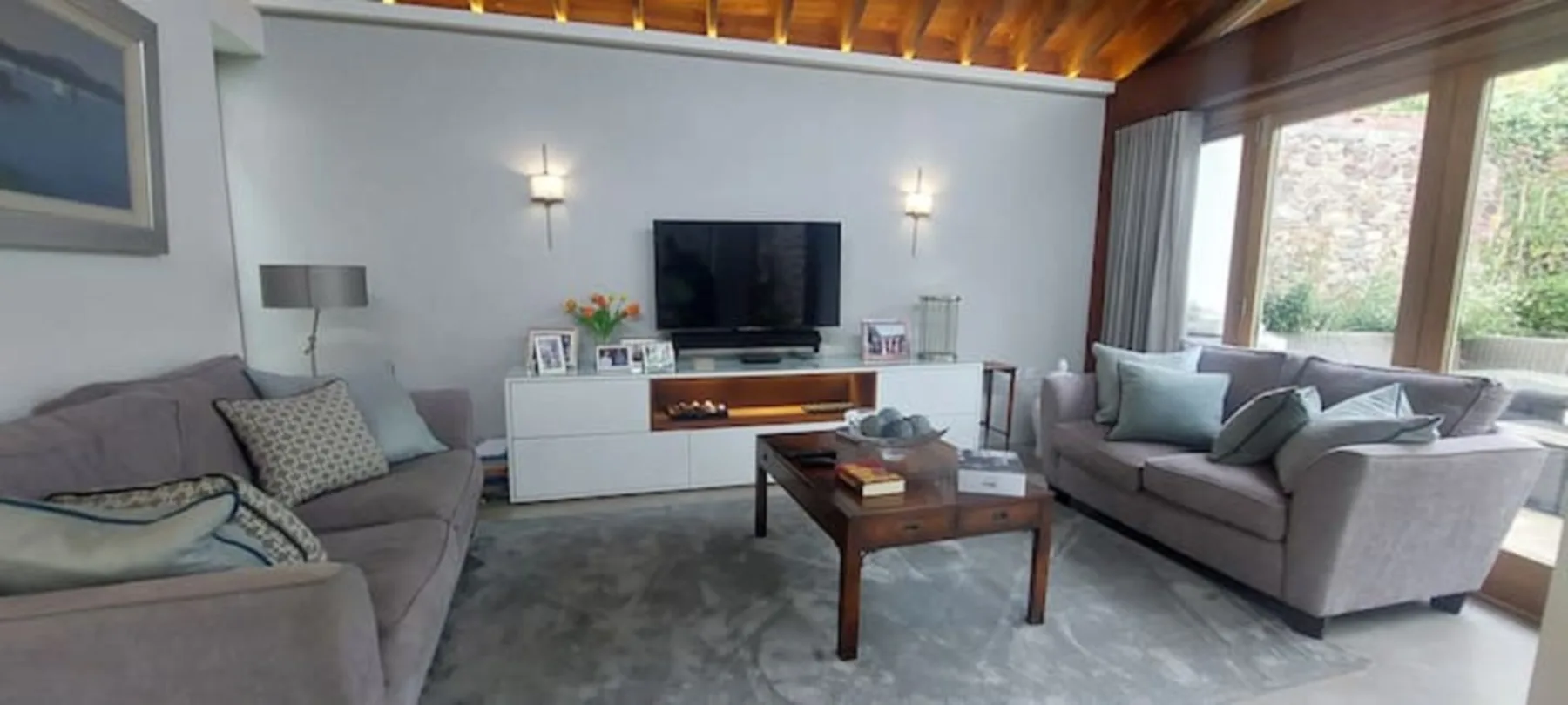 Sala de estar con asientos, un televisor y ventanas grandes.