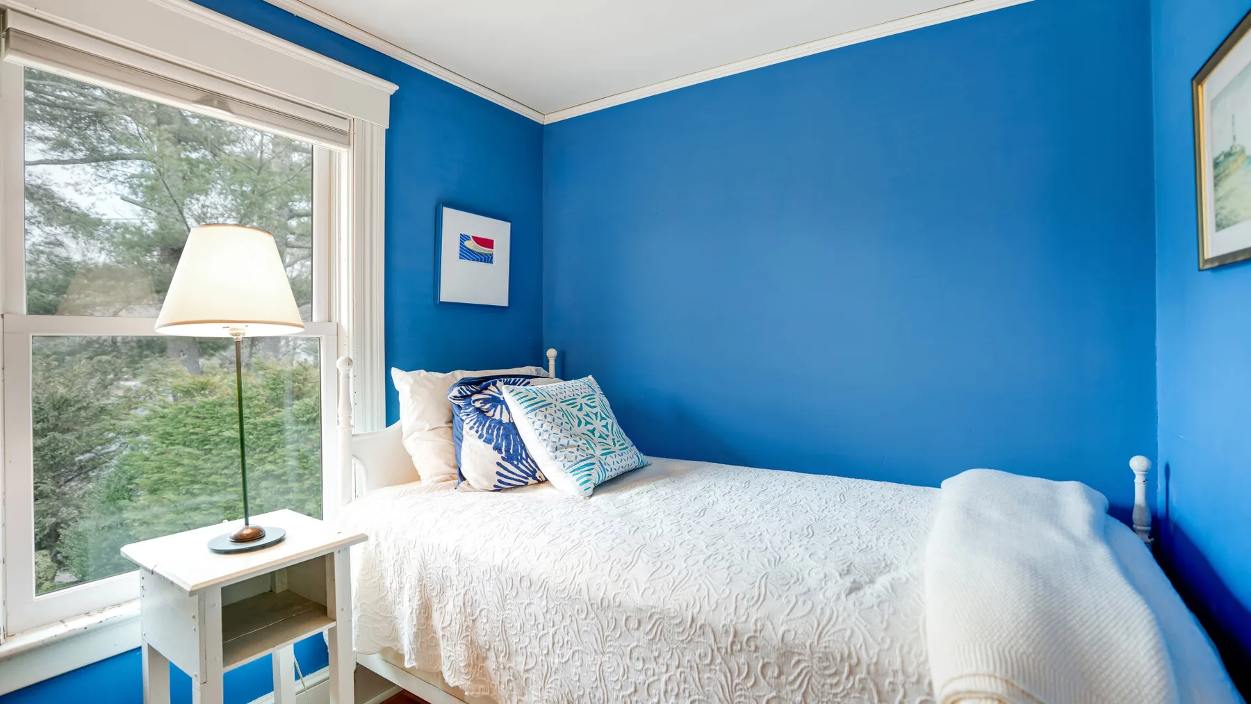 Un dormitorio luminoso con una cama blanca junto a una ventana grande.