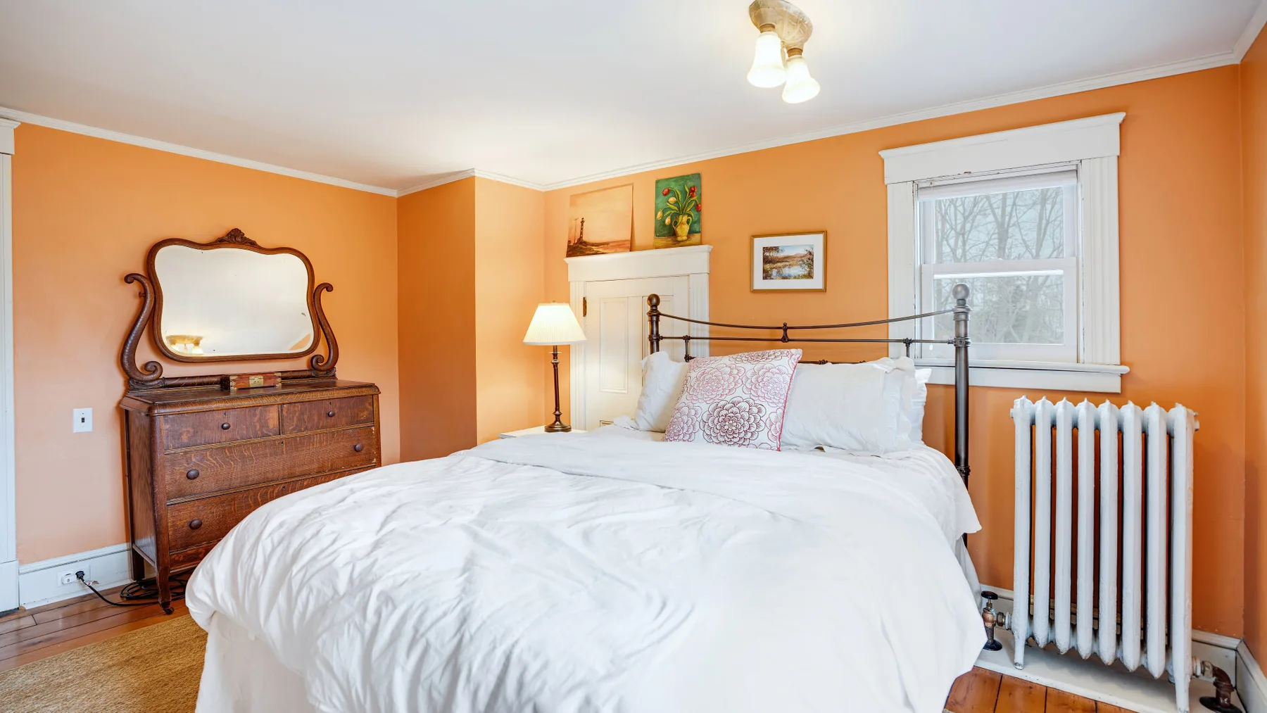 Un dormitorio con una cama blanca, una cómoda de madera y una ventana.
