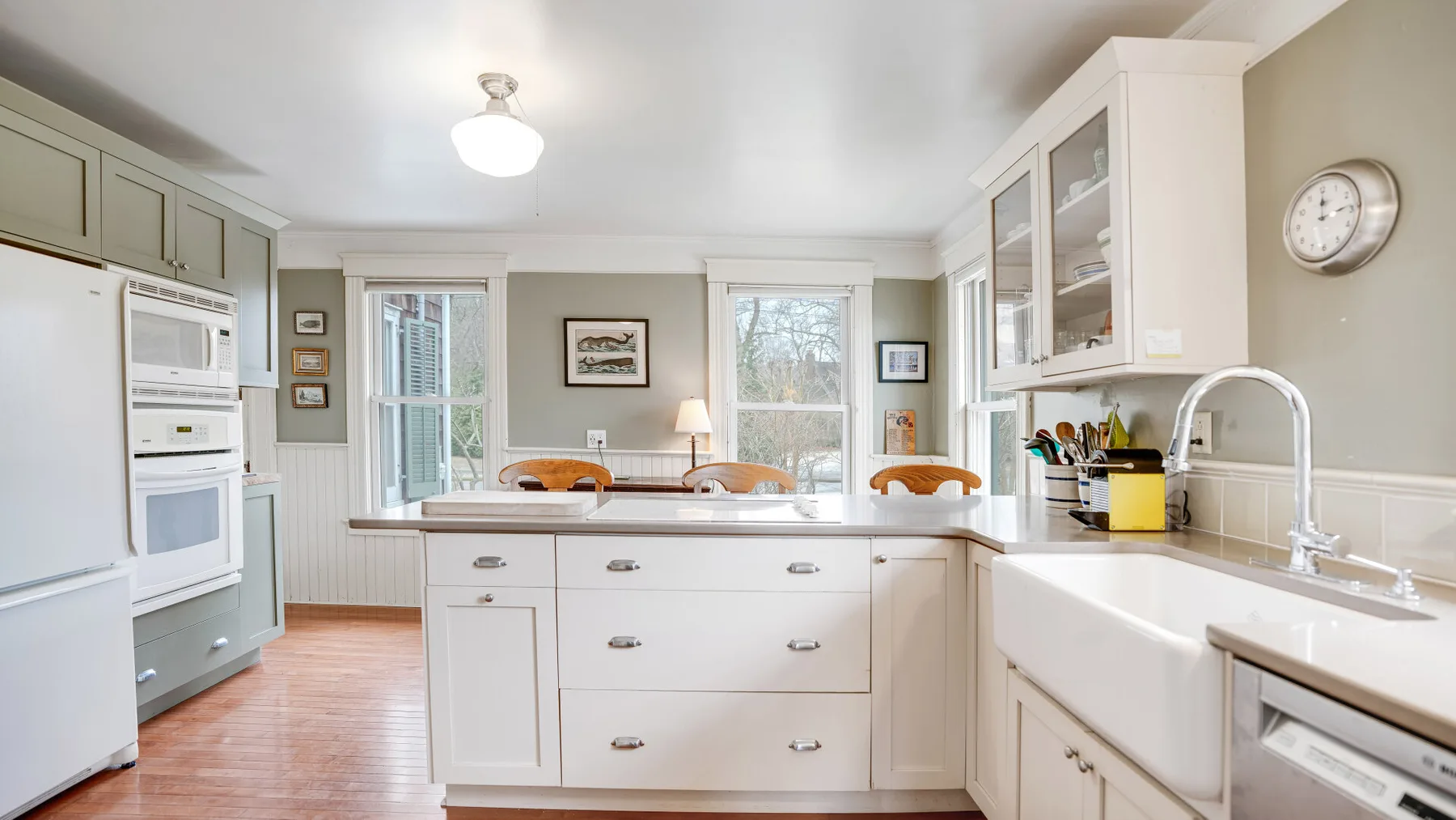 A bright kitchen with a central island, white cabinetry, and large windows.