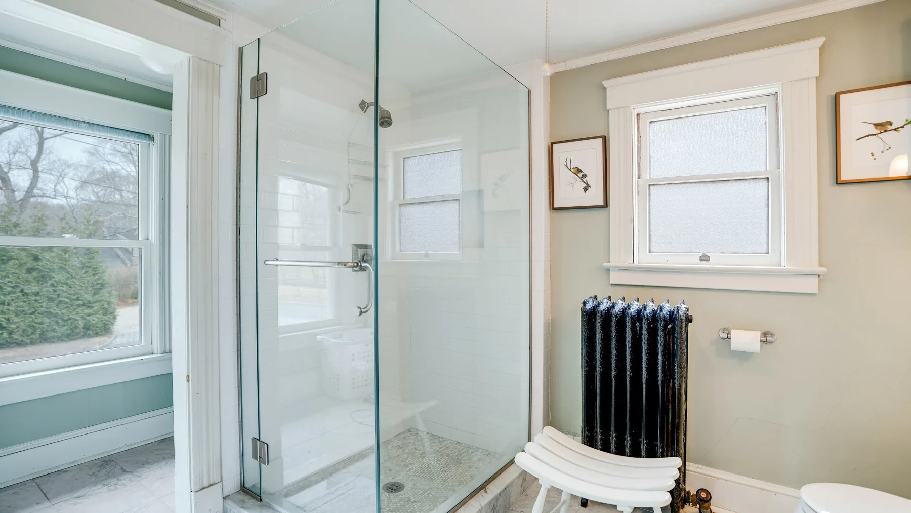 A bathroom with a glass shower, a window, and a radiator.