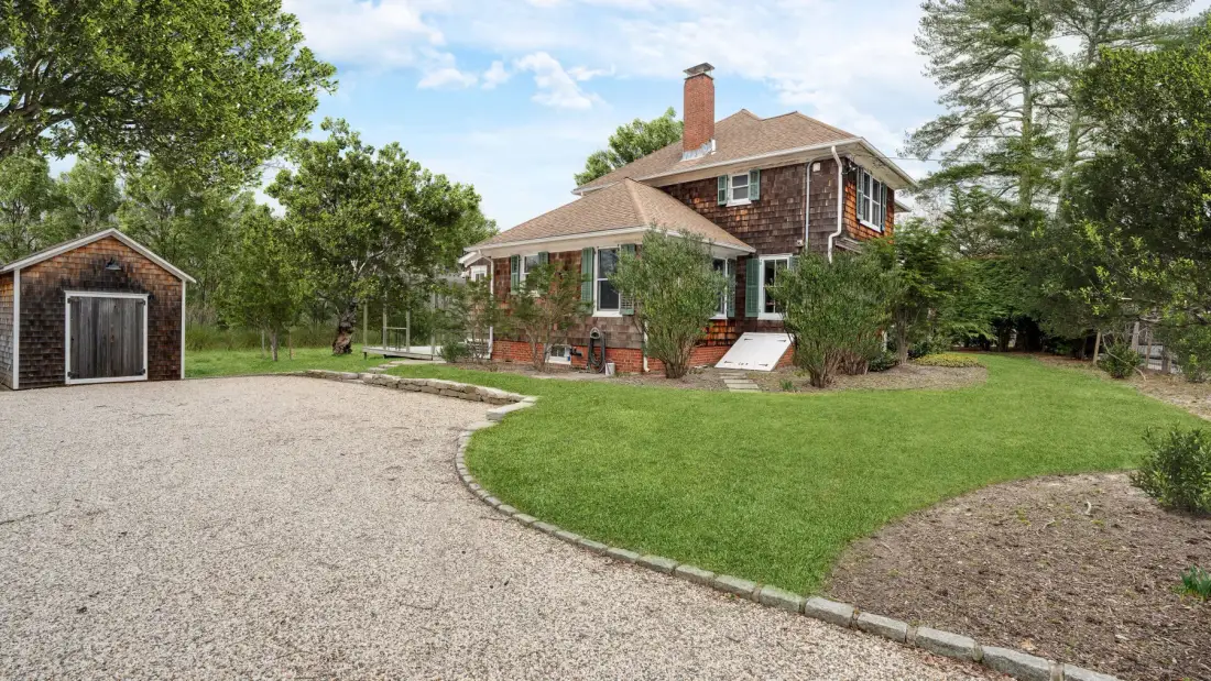Una casa de ladrillo de dos plantas está junto a una entrada curva de grava y un césped verde.