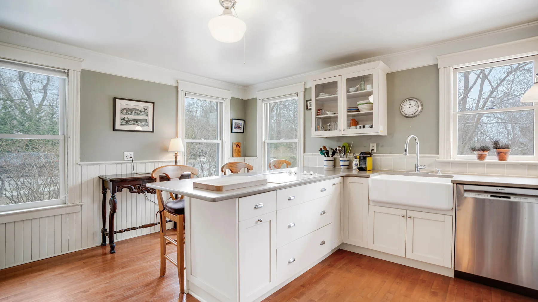 Una cocina luminosa con una isla central, gabinetes blancos y ventanas grandes.
