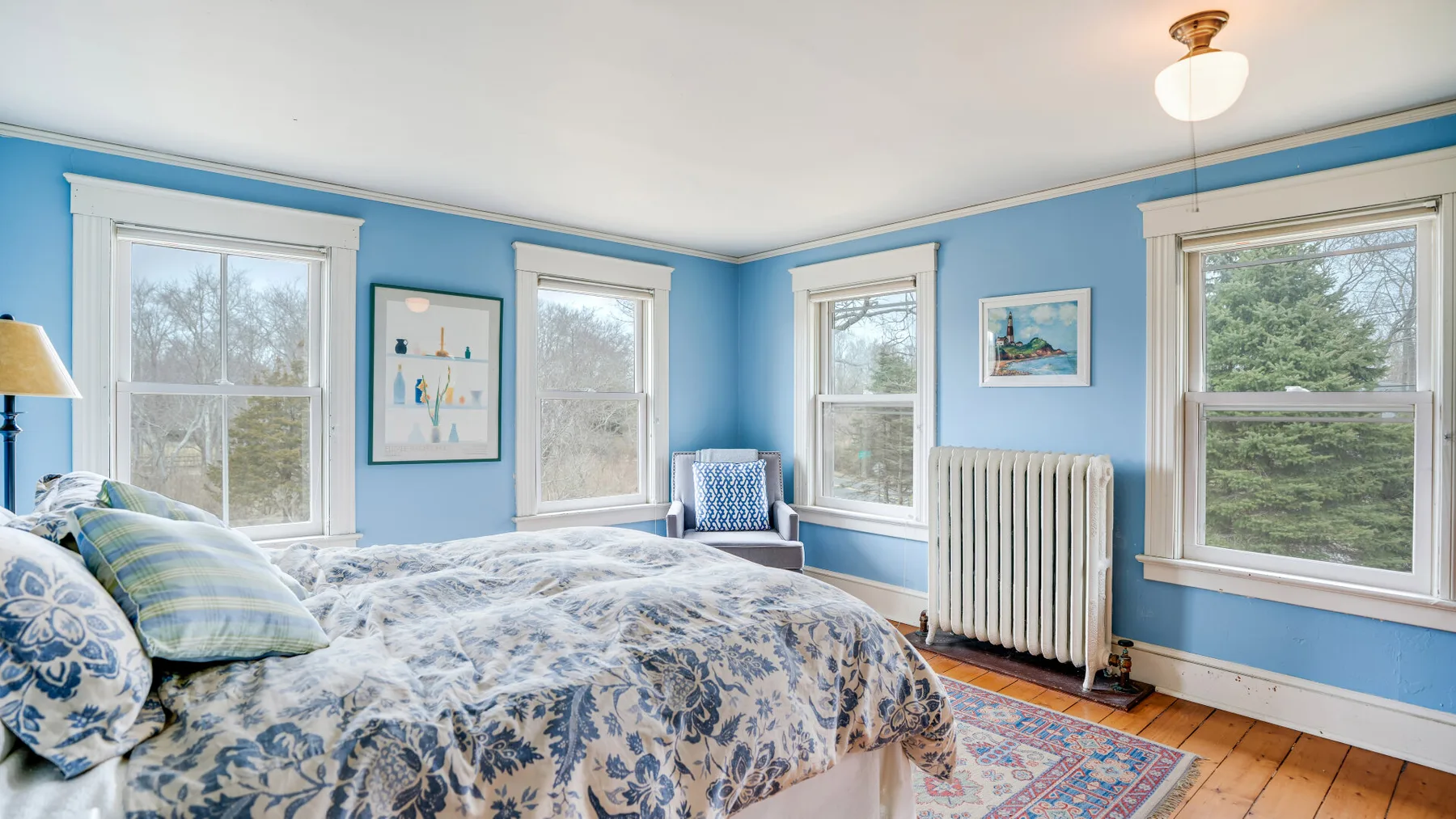 Un dormitorio azul con una cama, varias ventanas y un radiador.
