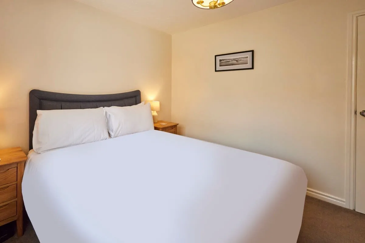 A bedroom with a bed, white bedding, and wooden bedside tables.