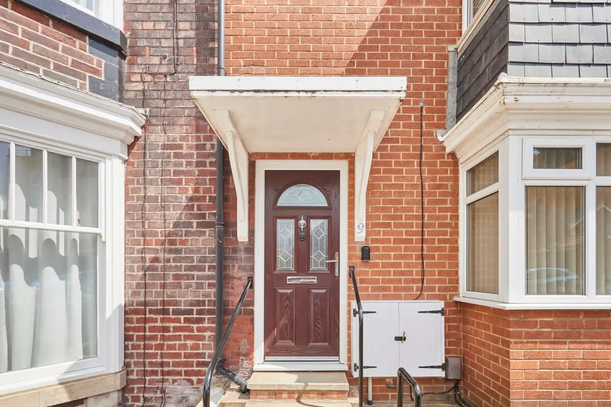 A brick building entrance with a dark wooden door and windows on either side.