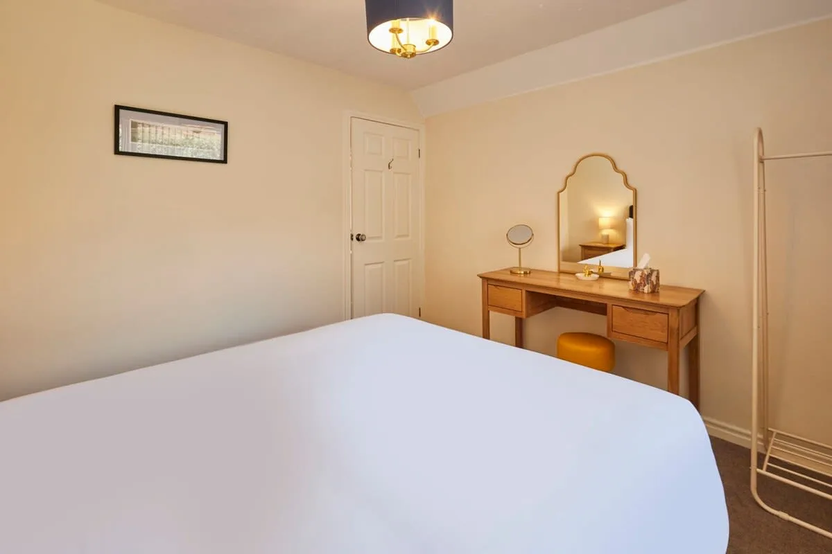 A bedroom with a bed and a wooden desk beneath a mirror.
