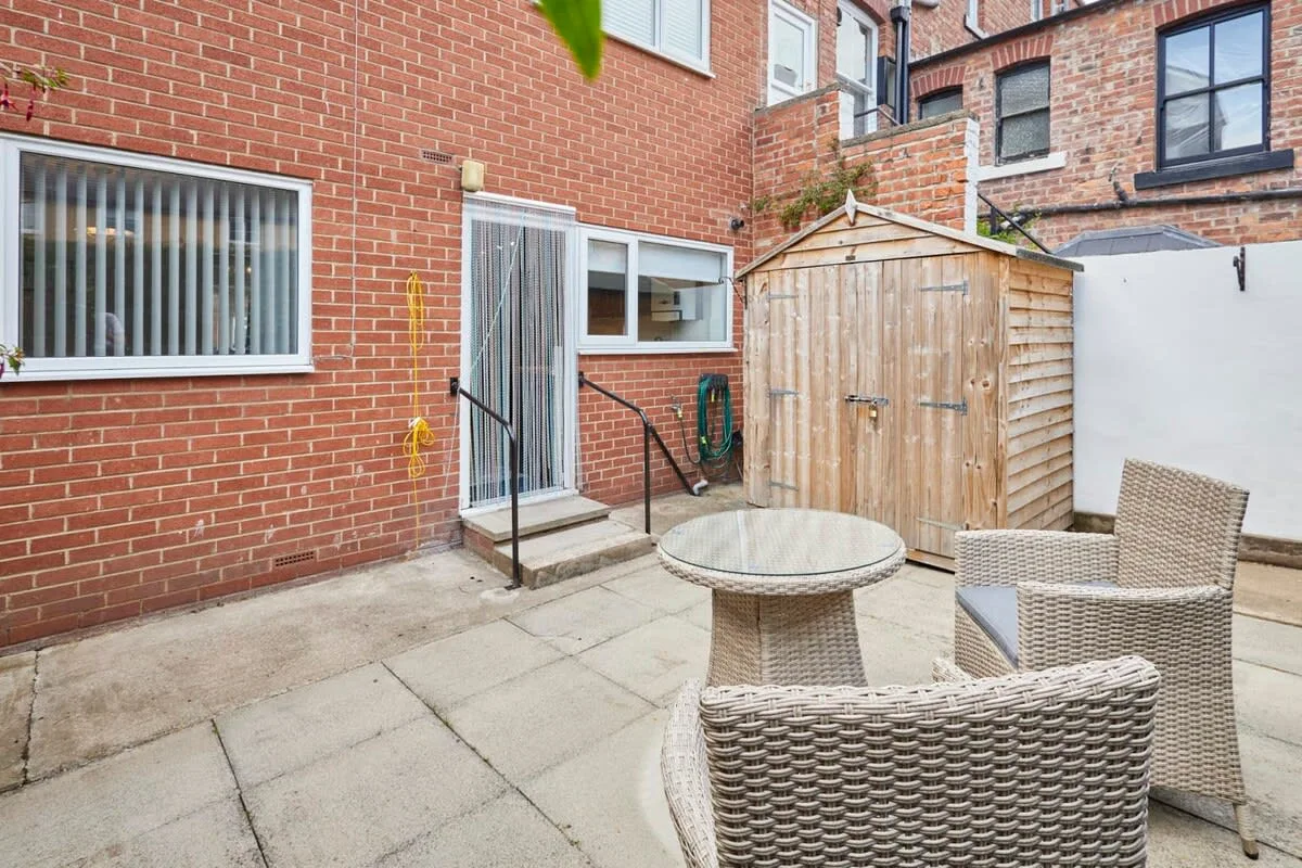 A paved outdoor patio with woven seating and a wooden shed.