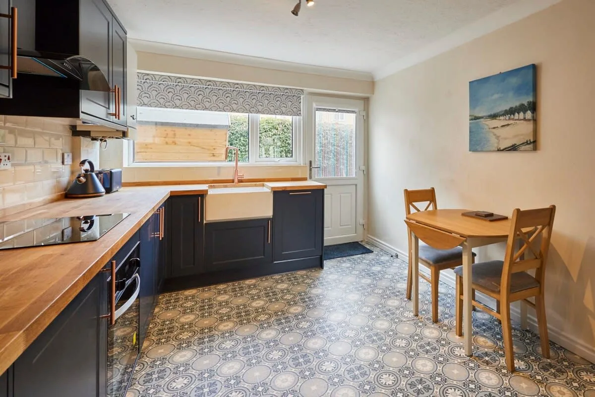 A kitchen with dark cabinets, a dining table, and windows along the back wall.