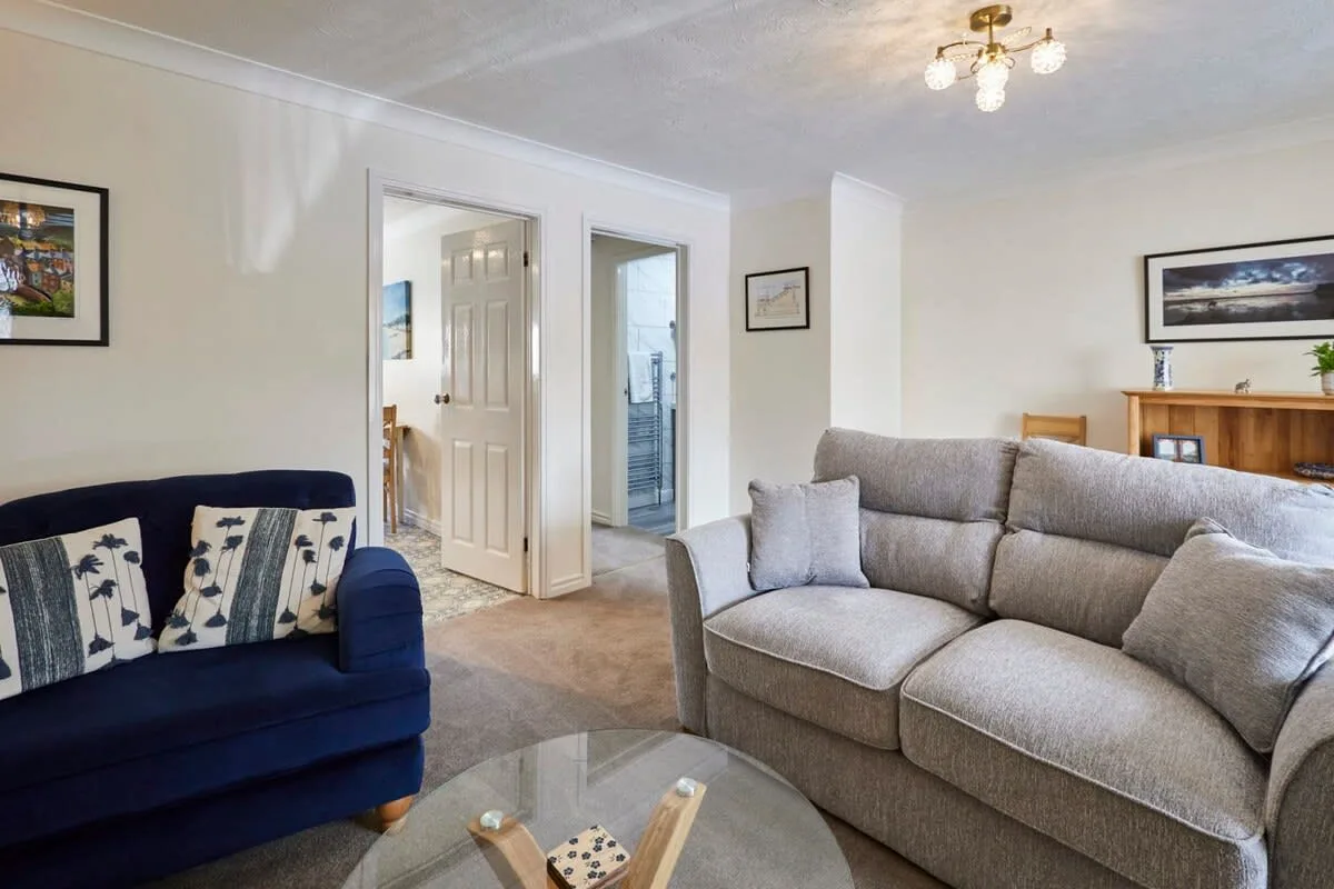 A living room with seating, a glass coffee table, and open doorways.